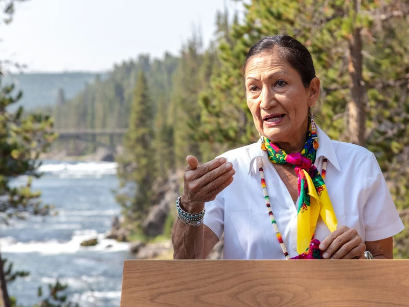 Photo of Secretary of the Interior Deb Haaland speaking at a podium outdoors in Yellowstone National Park.