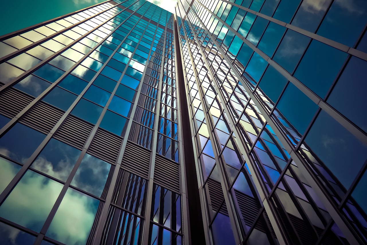 A tall glass building rising up to the sky with reflections