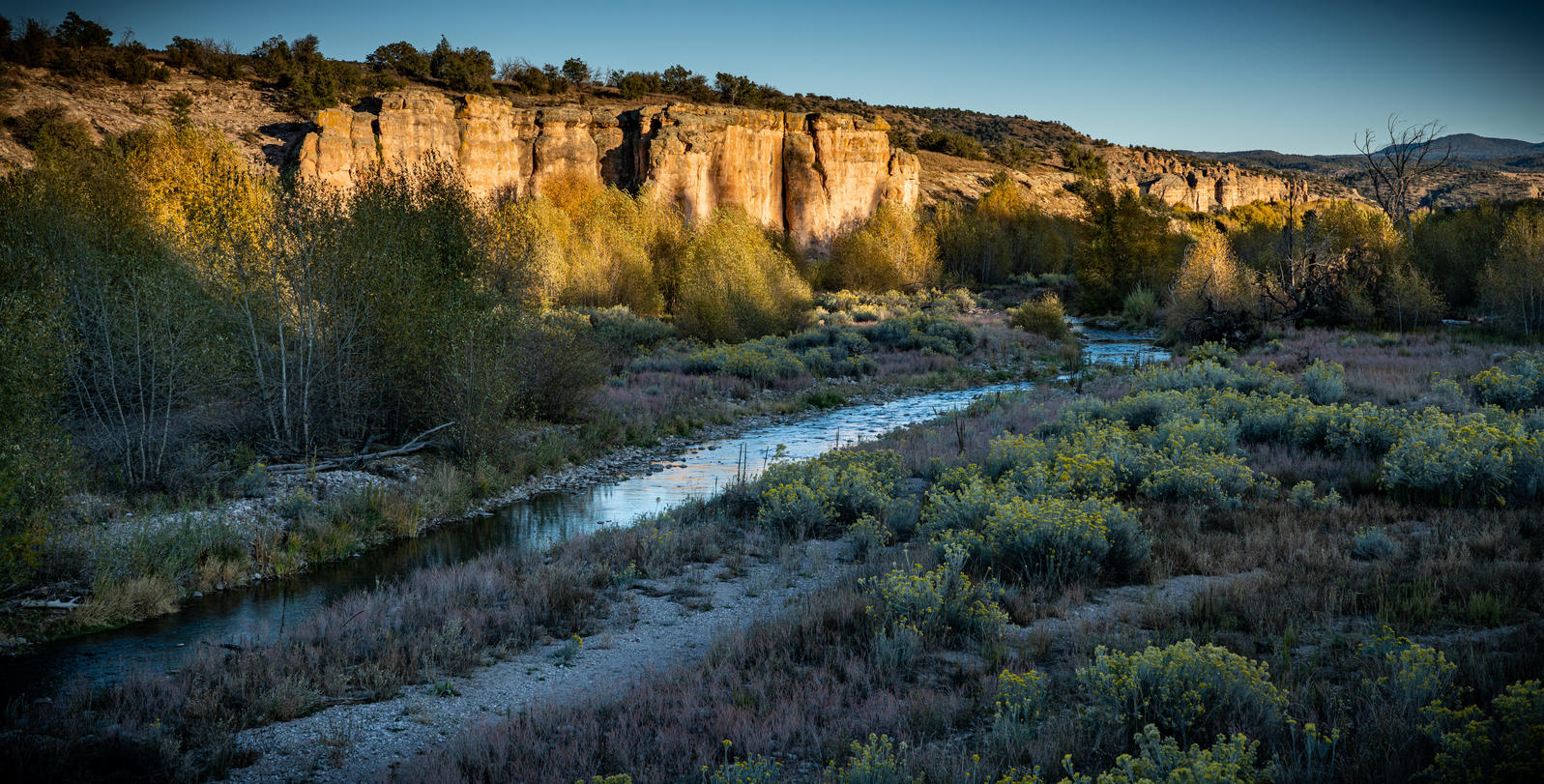 A stretch of the Gila River running next to a canyon hit by golden hour sunlight.