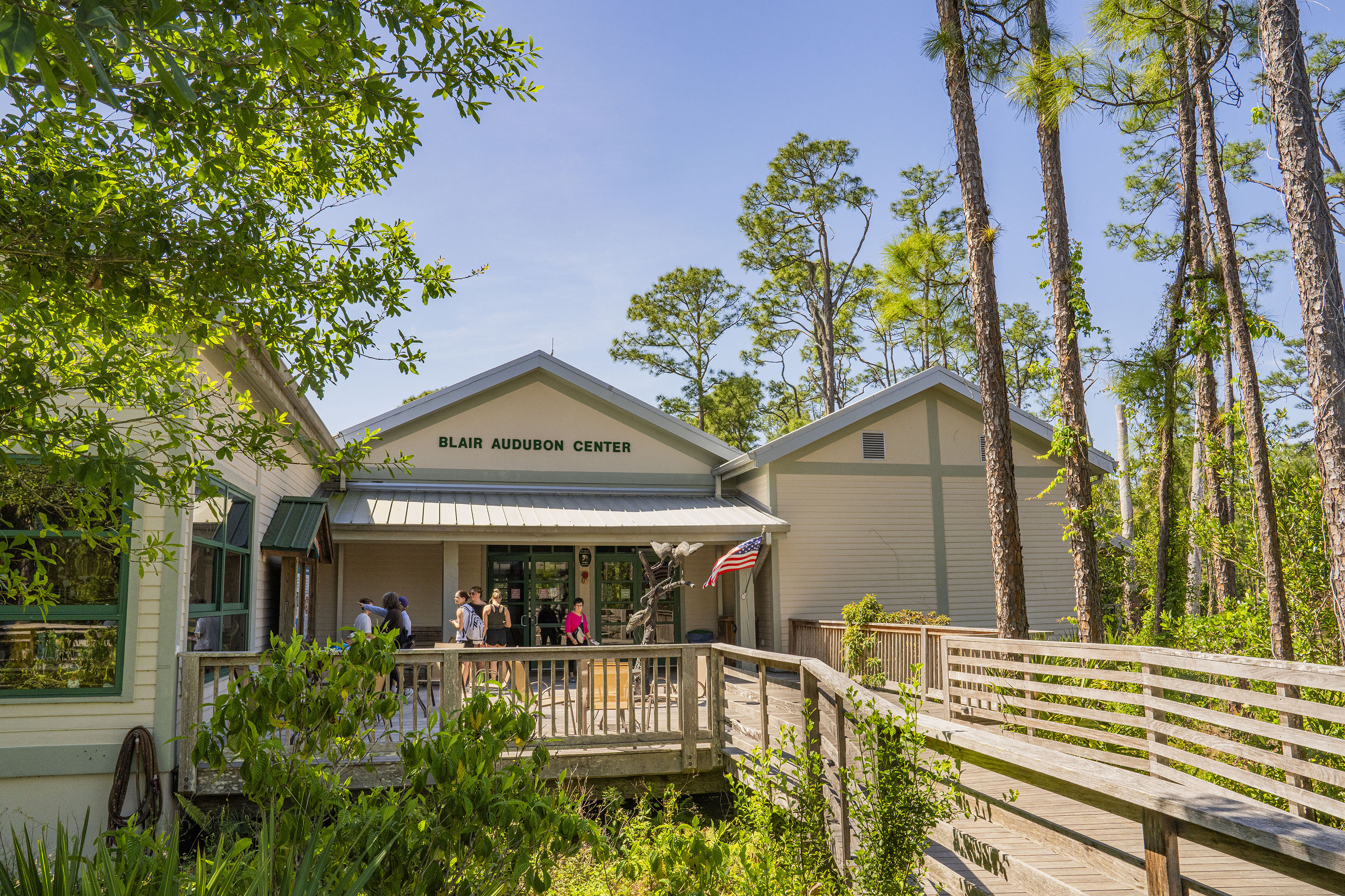 View of the front of a building with a boardwalk and people walking to the entrance where an American flag is waving.