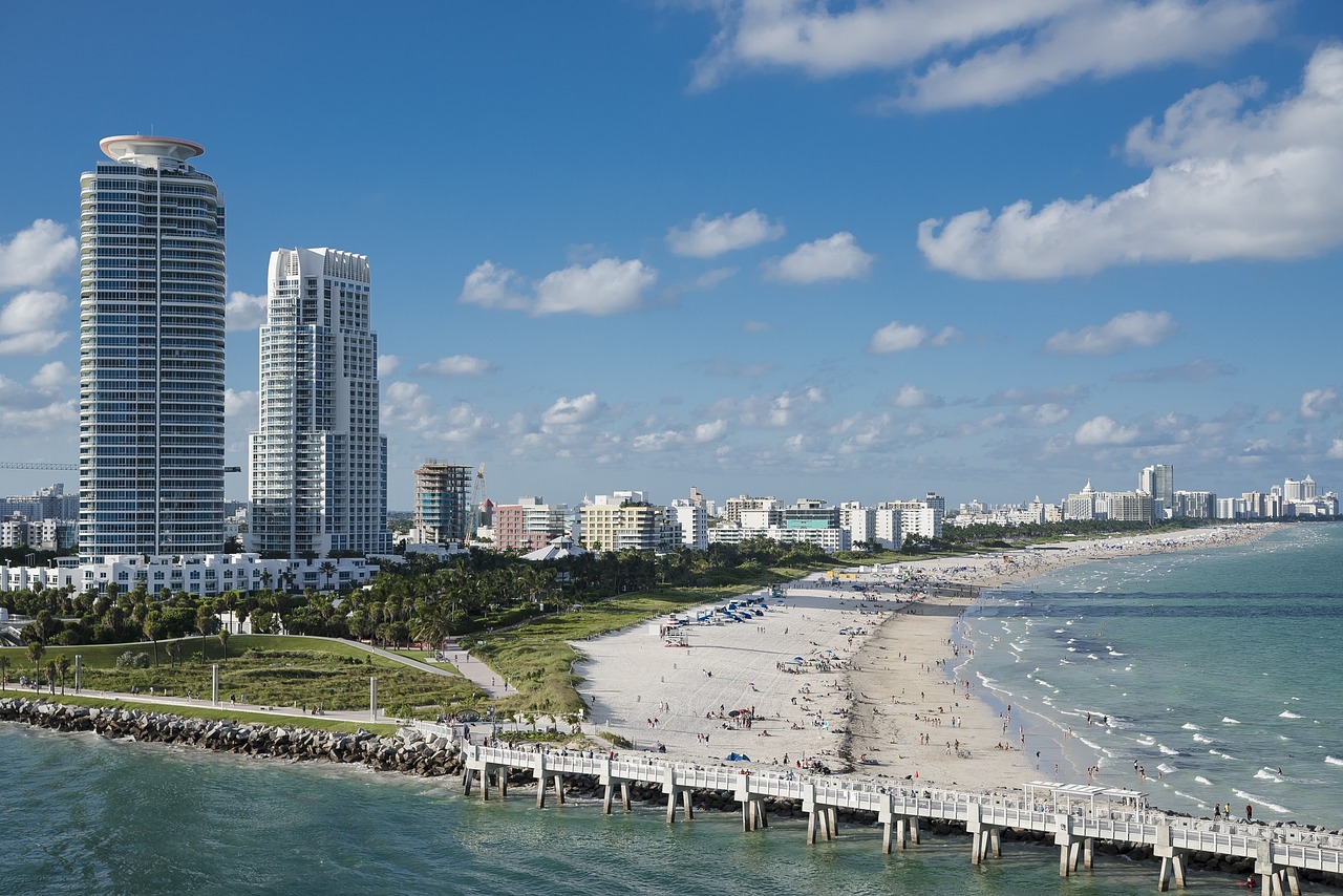 View of a waterway with a bridge, beach, and city beyond.