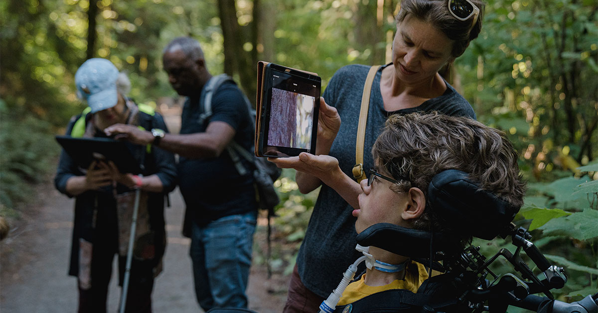 Lucas Hanson—who has limited mobility and vision because he was born with myotubular myopathy—looks at a nest on an iPad held by his mother, Krista Hanson, during a guided trek at Seward Park Audubon Center. 