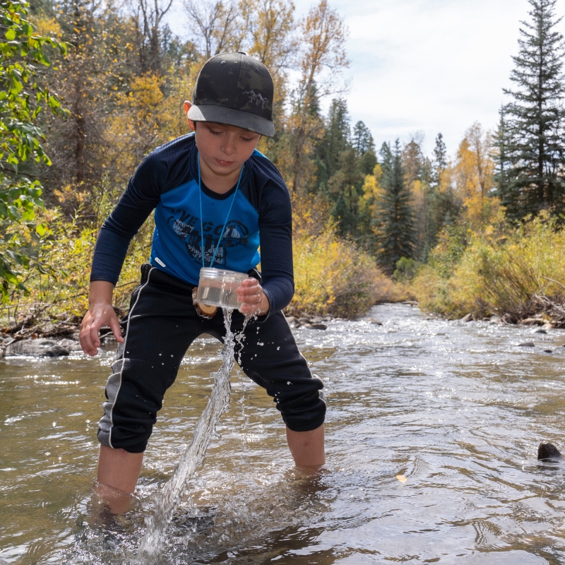 A child gathers water from a stream during a field trip.