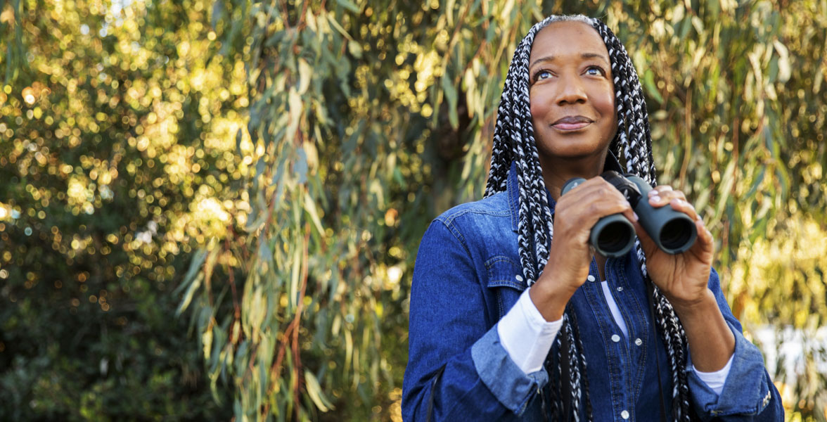 Tammah Watts stands outdoors with binoculars in her hands.