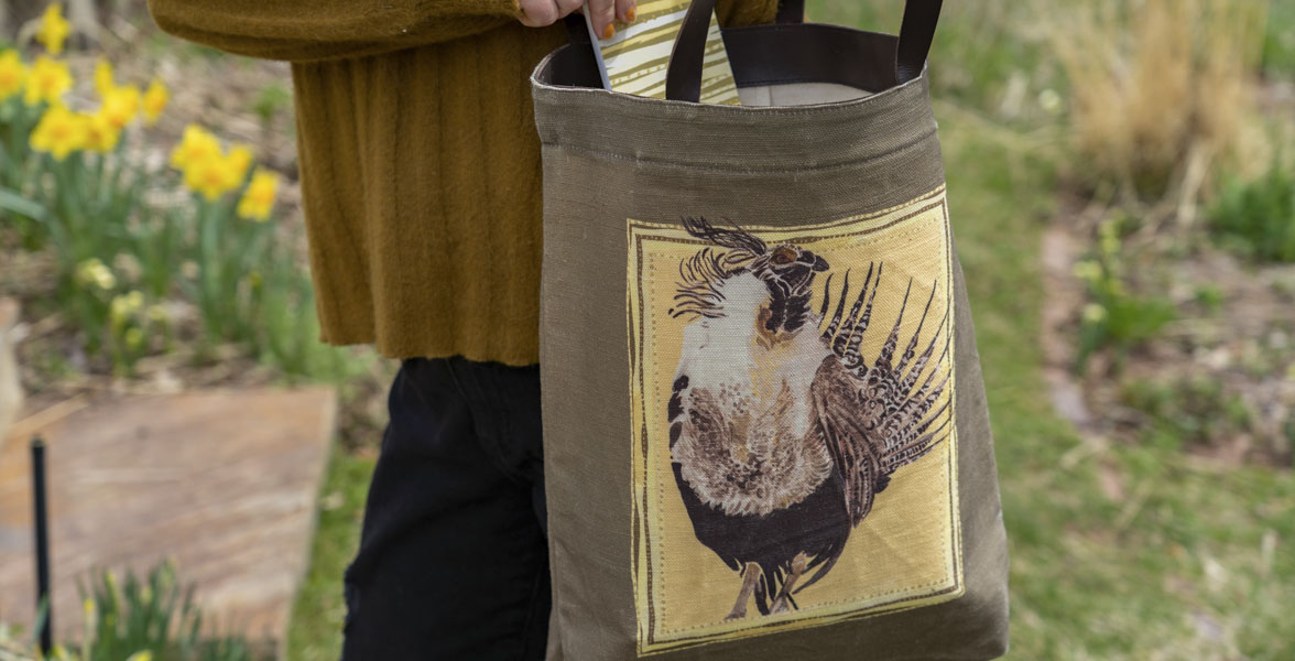 An adult holds a tote bag featuring artwork featuring the Gunnison Sage-Grouse. 