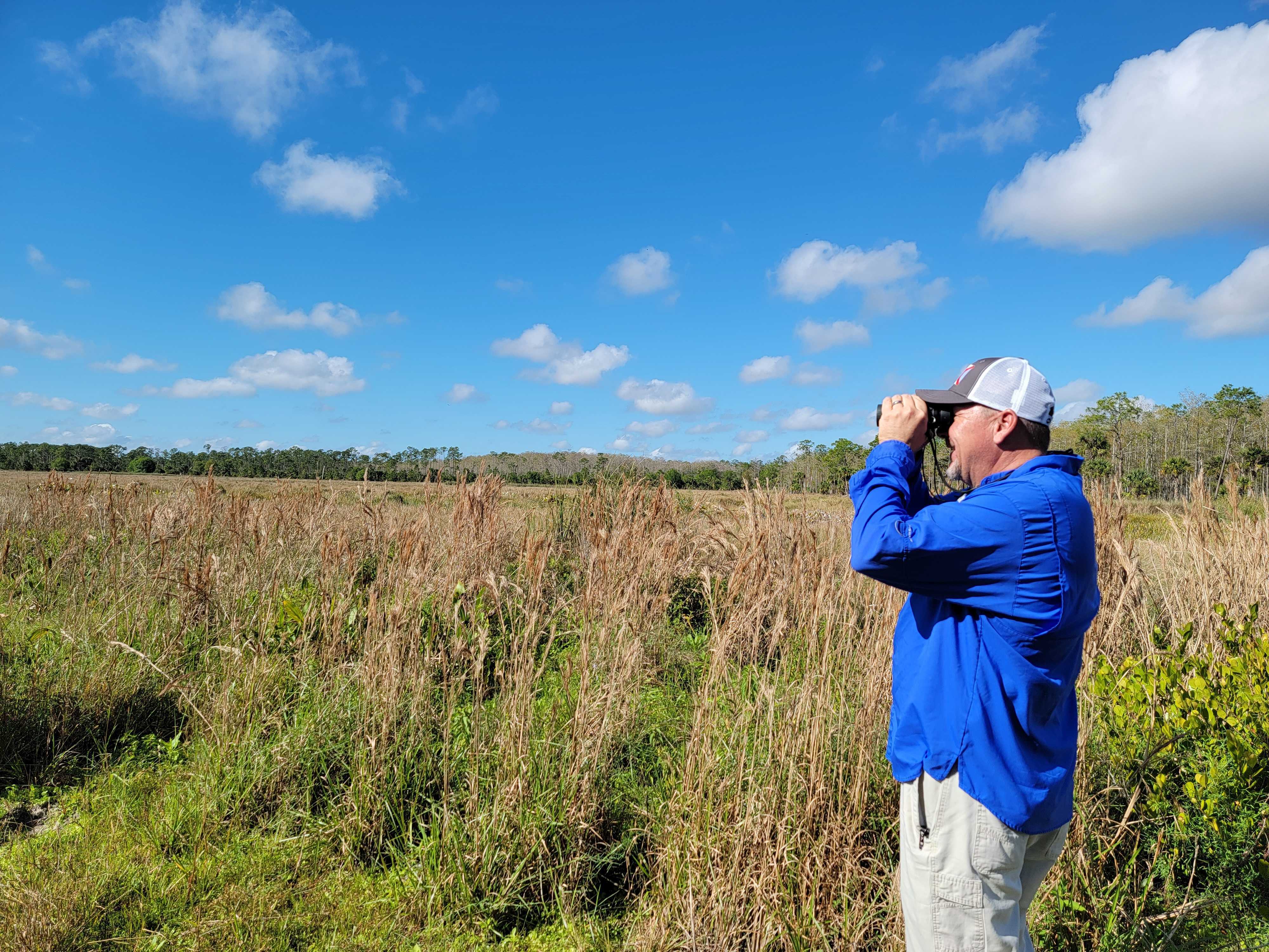A man with binoculars in a field.