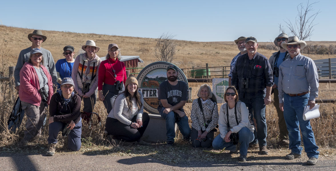 A group of adults stands around a sign at Rafter W Ranch.