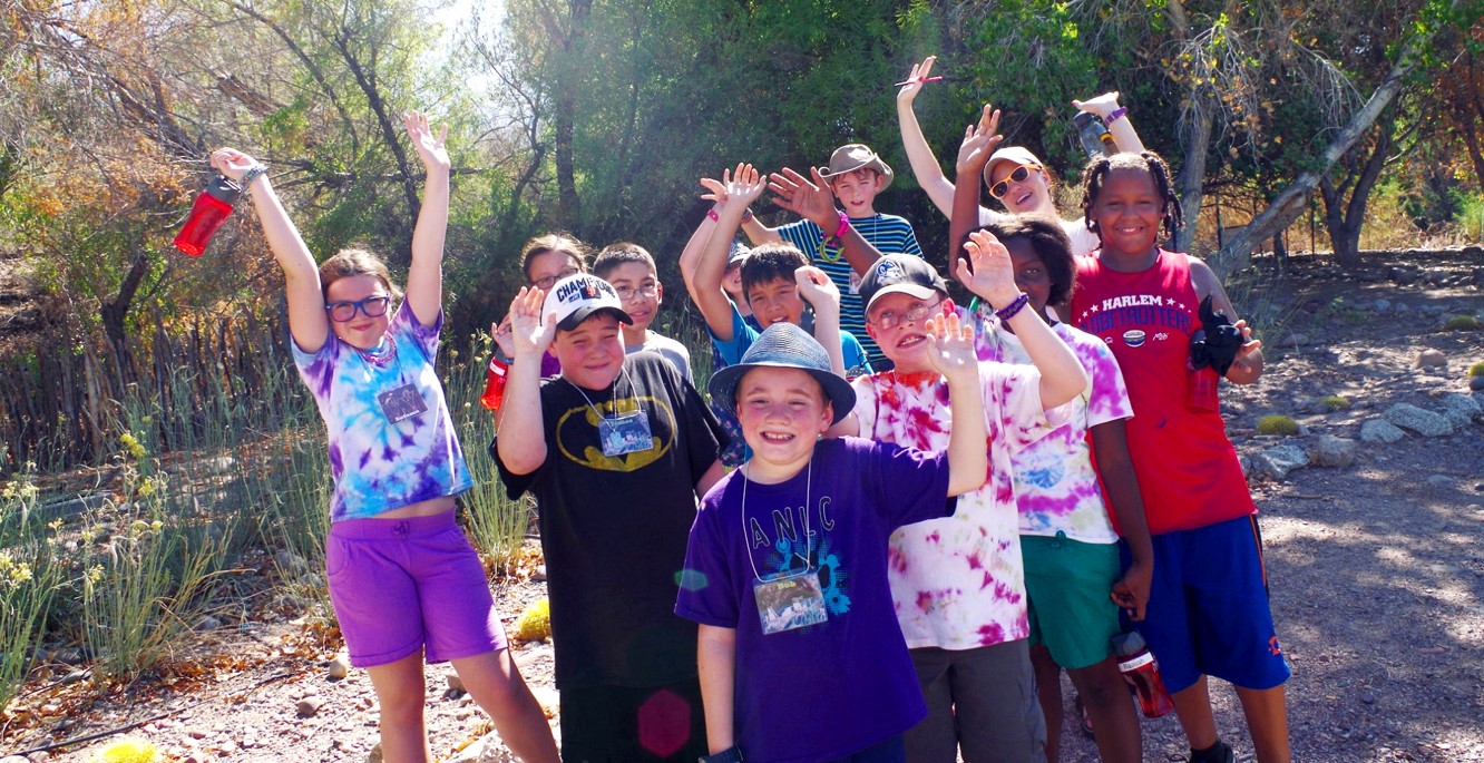 A group of camp kids excitedly pose next to a river.