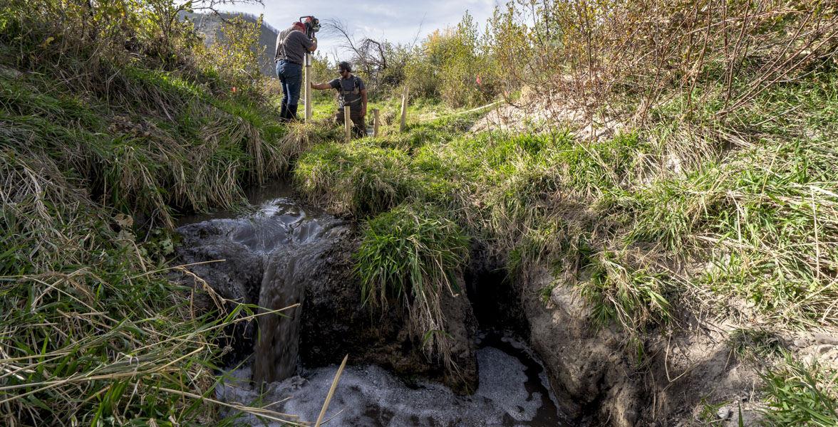 Two men pound wood posts into a creekbed.