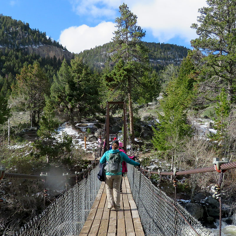 A person walks over a river towards mountains on a suspension bridge.