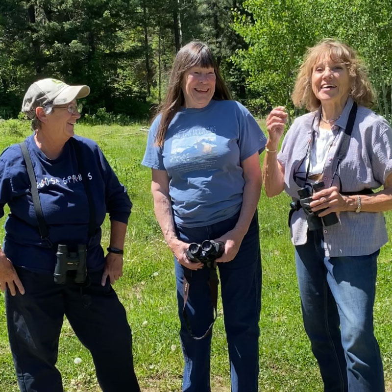 Three smiling adults stand in a line in a montane forest.