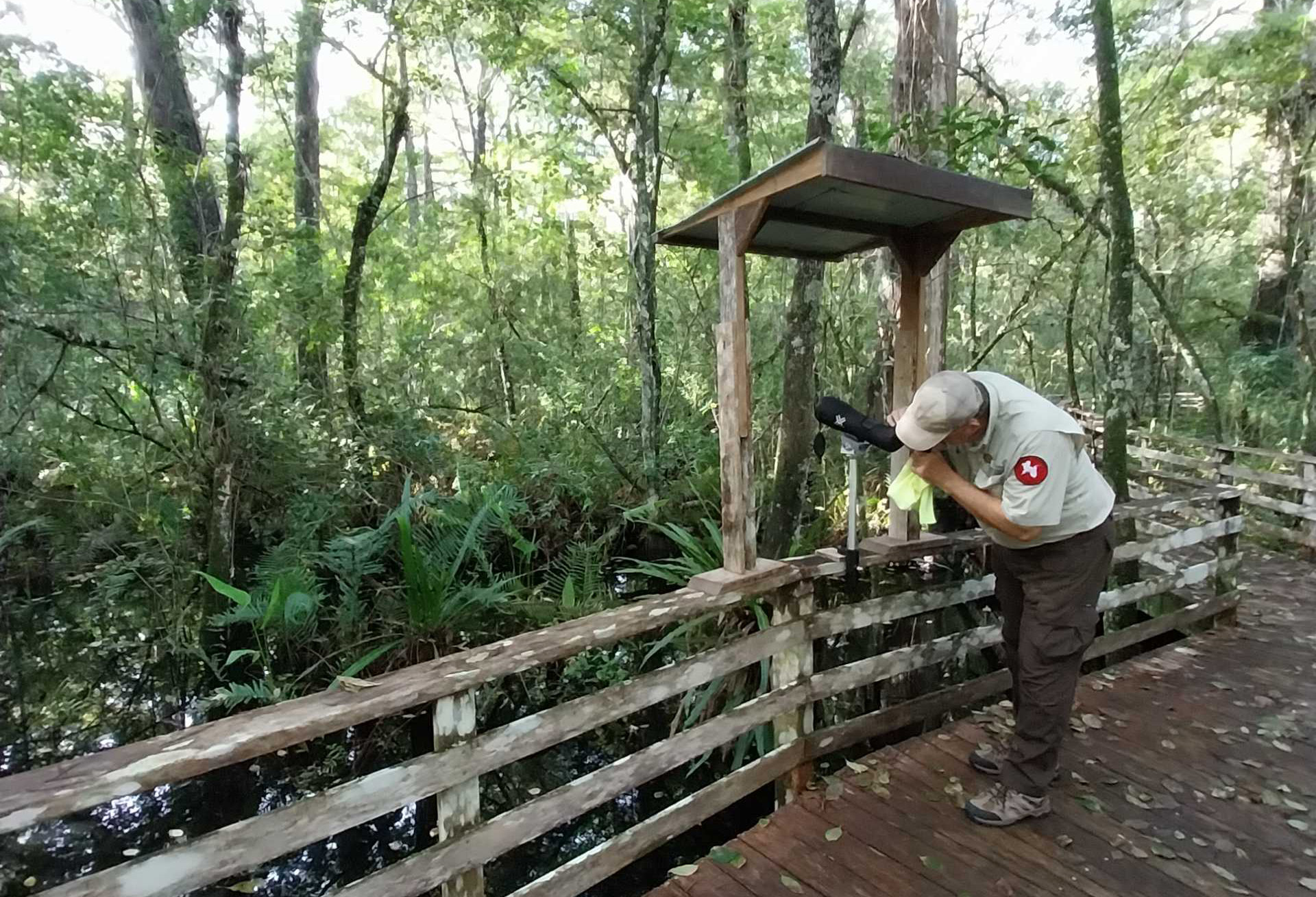 A man adjusting a scope on a boardwalk under a small roof